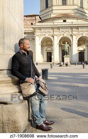 Stock Photo - tourist man rests leaning at one column of arcade in front of ancient church in city center, in background the square and the monumental entrance. Fotosearch