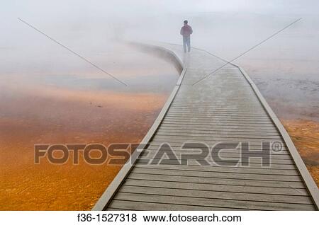 Stock Photo - Tourist on boardwalk in steam over the fragile ground at the Grand Prismatic Spring, Midway Geyser Basin, Yellowstone National Park, Wyoming. Fotosearch