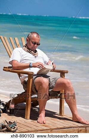 Stock Image - Tourist sitting in chair on beach reading book, Playa del Pablo, Little Corn Island, Corn Islands, Nicaragua. Fotosearch