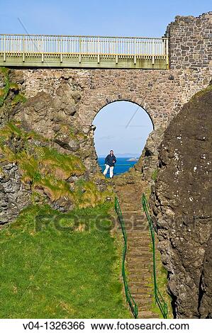 Stock Photograph - Tourist standing in the archway of the historic Dunluce Castle, Northern Ireland, Europe. Fotosearch
