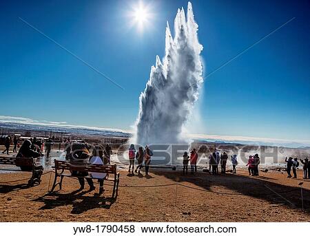Stock Photo - Tourist watching Strokkur geyser erupting, Iceland Strokkur is a fountain geyser in the geothermal area beside the Hvita River It is one of Iceland's most famous geysers, erupting about every 4-8 minutes 15 - 20 m high, sometimes up to 40 m high. Fotosearch