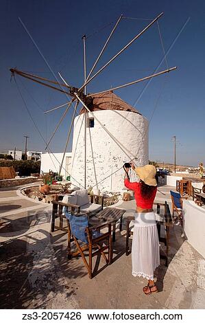 Stock Photograph - Tourist woman taking a photo of the windmill, Koufonissi, Cyclades Islands, Greek Islands, Greece, Europe.. Fotosearch
