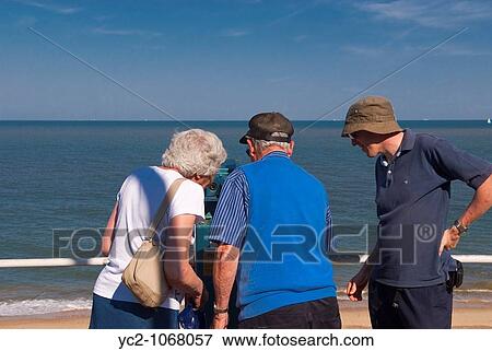 Stock Photo - Tourists looking through the pay to view binoculars on Southwold seafront in the Uk. Fotosearch
