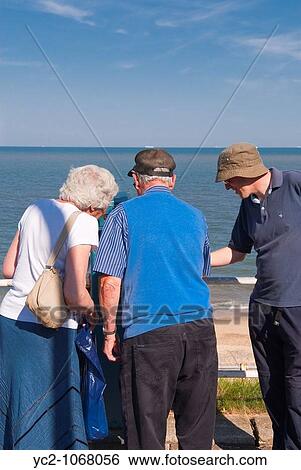 Tourists looking through the pay to view binoculars on Southwold seafront in the Uk View Large Photo Image Stock Photograph - Tourists looking through the pay to view binoculars on Southwold seafront in the Uk. Fotosearch