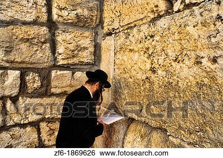Stock Photograph - Traditional men praying and prayer requests in the cracks at the famous religious Western Wall also called the Wailing Wall in Jerusalem Israel. Fotosearch