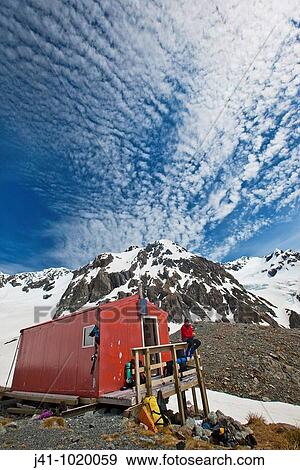 Stock Photo - Tramper outside Barker hut as high cloud forms overhead, Arthur's Pass National Park, Canterbury, New Zealand.. Fotosearch