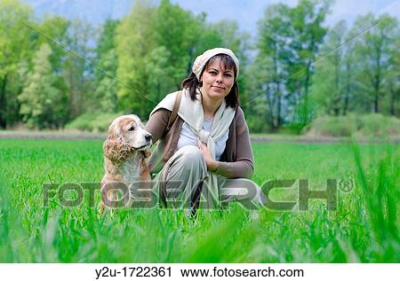 Stock Image - Travel woman with scarf and backpack on the green field with grass and trees and a dog. Fotosearch