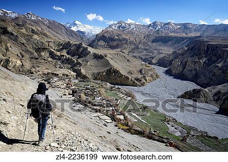 Stock Photo - Trekker going down towards the village of Tangge. Nepal, Gandaki, Upper Mustang (near the border with Tibet). Model Released.. Fotosearch