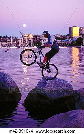 Picture - Trials mountain biker balancing on rock. Vancouver. Canada.. Fotosearch