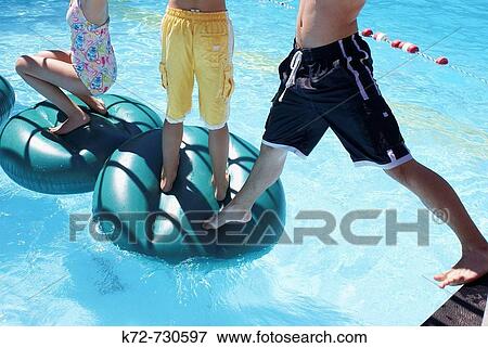 Stock Photo - Trying to step onto a floating platform and keep your balance in the water is quite a challenge. Fotosearch