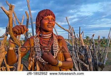 Stock Image - Turmi Ethiopia Africa Lower Omo Valley village with Bena Tribe First Wife smiling in sunset in wood hut village 24. Fotosearch