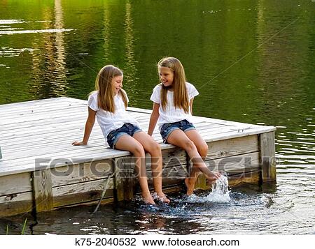 Twin sisters sitting on a dock on a lake View Large Photo Image Stock Image - Twin sisters sitting on a dock on a lake. Fotosearch