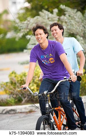 Stock Image - Twins riding tandem bike. Fotosearch