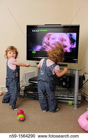 Stock Image - Twins watching TV at home. Fotosearch