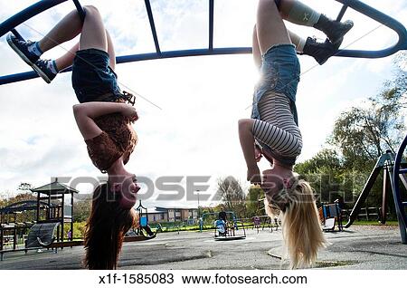 Stock Image - Two 16 17 year old teenage girls, hanging upside down in a playground, UK. Fotosearch