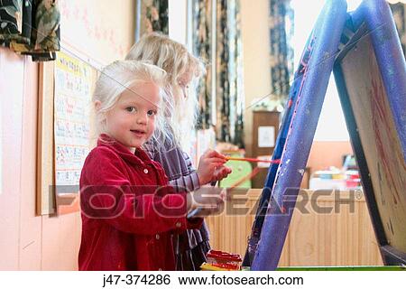 Two 3 year old girls standing at an easel, at nursrey school, painting View Large Photo Image Stock Photograph - Two 3 year old girls standing at an easel, at nursrey school, painting. Fotosearch