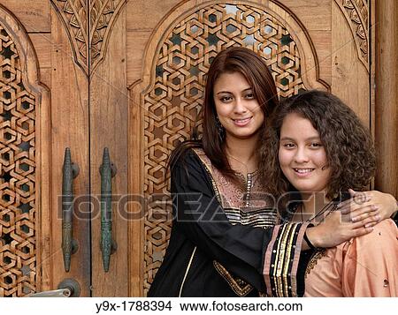 Picture - Two Arab Muslim Malaysian sisters standing in front of an intricately designed doorway. Fotosearch