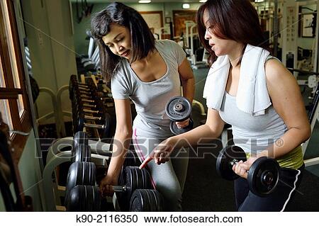 Stock Image - Two asian women busy choosing the right weight, Jakarta, Indonesia, Southeast Asia.. Fotosearch