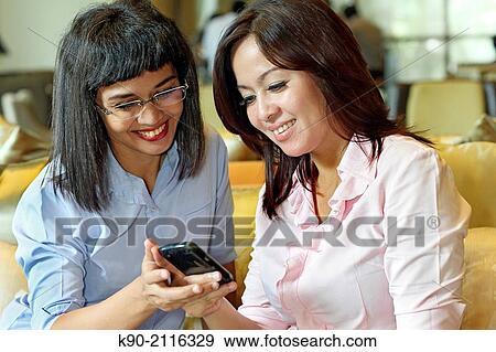 Two asian women holding a smartphone, Jakarta, Indonesia, Southeast Asia. View Large Photo Image Stock Photo - Two asian women holding a smartphone, Jakarta, Indonesia, Southeast Asia.. Fotosearch