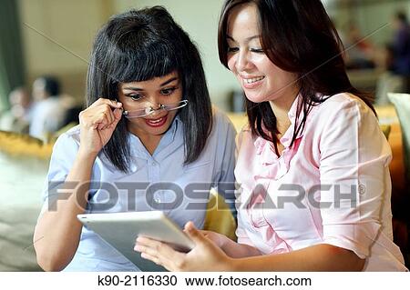 Stock Image - Two asian women holding a tablet computer, Jakarta, Indonesia, Southeast Asia.. Fotosearch