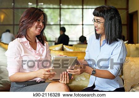 Two asian women holding a tablet computer, Jakarta, Indonesia, Southeast Asia. View Large Photo Image Stock Photo - Two asian women holding a tablet computer, Jakarta, Indonesia, Southeast Asia.. Fotosearch