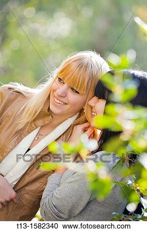 Stock Image - Two attractive young women are talking discreetly. Fotosearch