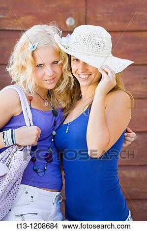 Picture - Two attractive young women pose before a wooden doors house entrance. Fotosearch