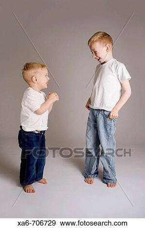 Two blond haired brothers, 6 and 3 years old, wearing white t-shirts and blue jeans, look at each other and laugh, sharing a joke. Studio lighting, grey background. View Large Photo Image Stock Photo - Two blond haired brothers, 6 and 3 years old, wearing white t-shirts and blue jeans, look at each other and laugh, sharing a joke. Studio lighting, grey background.. Fotosearch