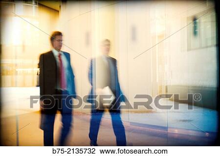 Two blured executives walking down the corridor of an office with documents in hand viewed through a glass in London, England, UK, Europe. View Large Photo Image Stock Image - Two blured executives walking down the corridor of an office with documents in hand viewed through a glass in London, England, UK, Europe.. Fotosearch