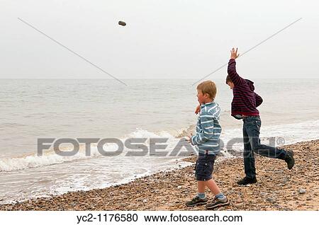 Stock Image - two boys 6 & 10 throwing stones into the sea on a UK beach. Fotosearch