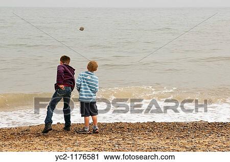 Stock Image - two boys 6 & 10 throwing stones into the sea on a UK beach. Fotosearch
