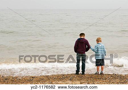 Stock Image - two boys 6 & 10 throwing stones into the sea on a UK beach. Fotosearch