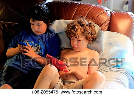Two boys aged 7 and 9 sitting on a sofa using an apple ipod touch and a 7 inch tablet to play games View Large Photo Image Stock Photography - Two boys aged 7 and 9 sitting on a sofa using an apple ipod touch and a 7 inch tablet to play games. Fotosearch