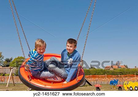 Stock Photo - Two boys on a swing at the play park in Westleton, Suffolk, England, Britain, Uk. Fotosearch