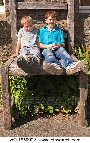 Two boys sit on the giant chair outside the Old School Crafts Shop and Gallery at Muker in Swaledale in North Yorkshire, England, Britain, Uk View Large Photo Image Stock Image - Two boys sit on the giant chair outside the Old School Crafts Shop and Gallery at Muker in Swaledale in North Yorkshire, England, Britain, Uk. Fotosearch