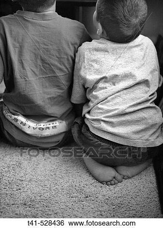 Two brothers sit side by side as they play video games and stare at the television. View Large Photo Image Stock Photograph - Two brothers sit side by side as they play video games and stare at the television.. Fotosearch
