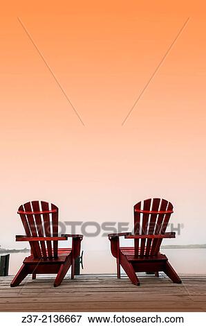 Stock Photo - Two chairs on a deck overlooking the ocean, Halifax, Canada, under a saffron sky. Fotosearch