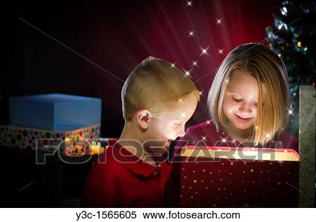 Stock Photography - Two children, boy and girl, enjoying the magic of Christmas while opening a present. Fotosearch