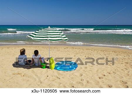 Two children looking out to sea while sitting under a parasol on a sunny beach in summer View Large Photo Image Stock Photography - Two children looking out to sea while sitting under a parasol on a sunny beach in summer. Fotosearch