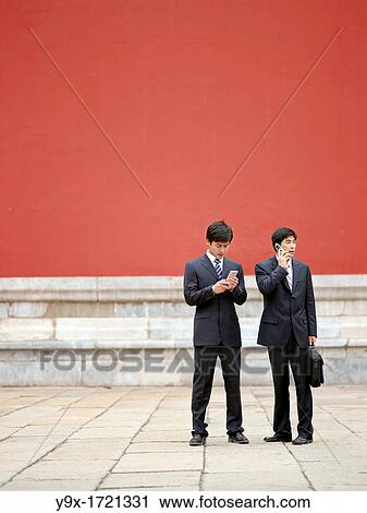 Two Chinese businessmen in suits, holding documents, having a discussion while on the phone in the Forbidden City View Large Photo Image Stock Image - Two Chinese businessmen in suits, holding documents, having a discussion while on the phone in the Forbidden City. Fotosearch