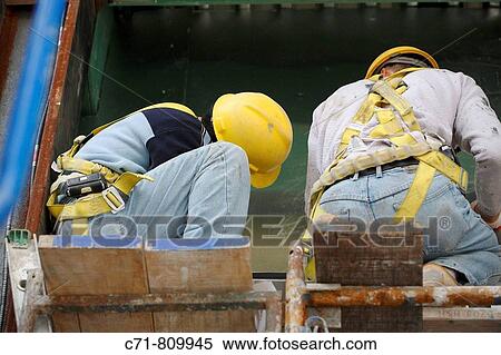Stock Photography - Two construction workers working on scaffolding. Fotosearch