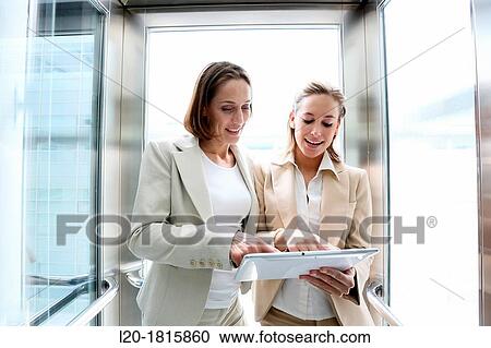 Two executives in elevator, using a digital tablet View Large Photo Image Stock Image - Two executives in elevator, using a digital tablet. Fotosearch