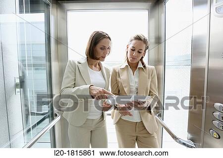 Two executives in elevator, using a digital tablet View Large Photo Image Stock Image - Two executives in elevator, using a digital tablet. Fotosearch
