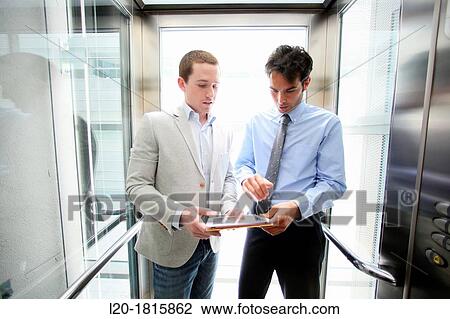 Two executives in elevator, using a digital tablet View Large Photo Image Stock Image - Two executives in elevator, using a digital tablet. Fotosearch