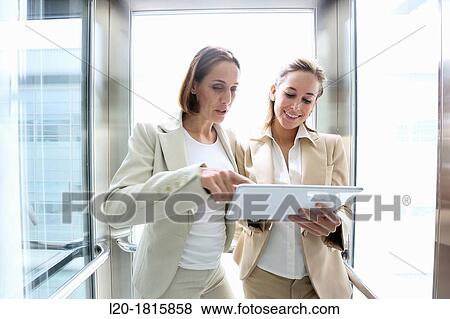 Two executives in elevator, using a digital tablet View Large Photo Image Stock Photo - Two executives in elevator, using a digital tablet. Fotosearch