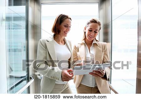 Two executives in elevator, using a digital tablet View Large Photo Image Stock Photo - Two executives in elevator, using a digital tablet. Fotosearch