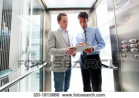 Two executives in elevator, using a digital tablet View Large Photo Image Stock Photograph - Two executives in elevator, using a digital tablet. Fotosearch