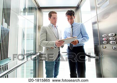 Two executives in elevator, using a digital tablet View Large Photo Image Stock Photography - Two executives in elevator, using a digital tablet. Fotosearch