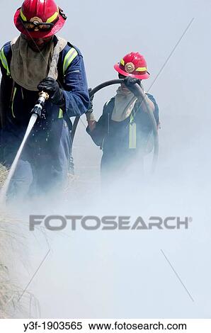 two firefighters, surrounded by thick smoke, using a fire hose, damp down a fire, View Large Photo Image Stock Photography - two firefighters, surrounded by thick smoke, using a fire hose, damp down a fire,. Fotosearch