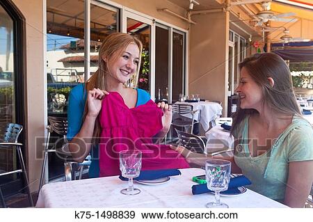 Two friends at outdoor cafe showing off new purchase View Large Photo Image Stock Photo - Two friends at outdoor cafe showing off new purchase. Fotosearch